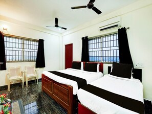 A hotel room with two beds, a desk, chairs, a ceiling fan, and windows with bars. - Saver Double Ruthran Guest House (Tirukalukundram)