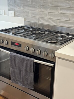 Une cuisine équipée d’une cuisinière, d’un four et d’un plan de travail en acier inoxydable, le tout agrémenté d’un pare-feu carrelé.
