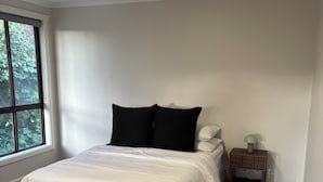 Un dormitorio con cama, mesita de noche, lámpara y ventana con vistas a zonas verdes.