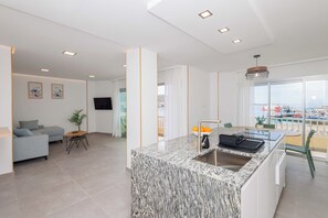 A modern kitchen with a granite countertop, a dining area with a table and chairs, a sofa, and a television. - Luxury beachfront apartment in the heart of Los Cristianos (Arona)
