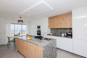 A modern kitchen with a central island, wooden cabinets, and a view through large windows. - Luxury beachfront apartment in the heart of Los Cristianos (Arona)