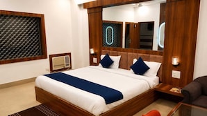 Une chambre d’hôtel moderne avec un grand lit, une tête de lit en bois, une table de chevet avec une lampe, un fauteuil rouge et une table basse en verre.