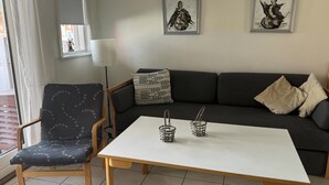 Una sala de estar con un sofá oscuro, un sillón estampado, una mesa blanca y dos obras de arte colgadas en la pared.