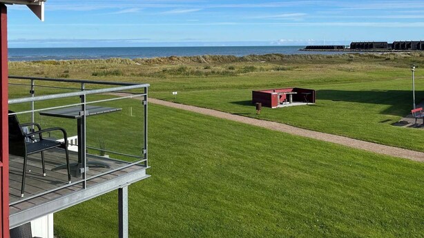 Un balcón con mesa y sillas, un campo cubierto de césped y una vista distante del mar.