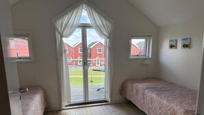 Una habitación con techo inclinado, dos camas con ropa de cama estampada, un ventanal corredera que da al exterior y una pequeña ventana en la pared.