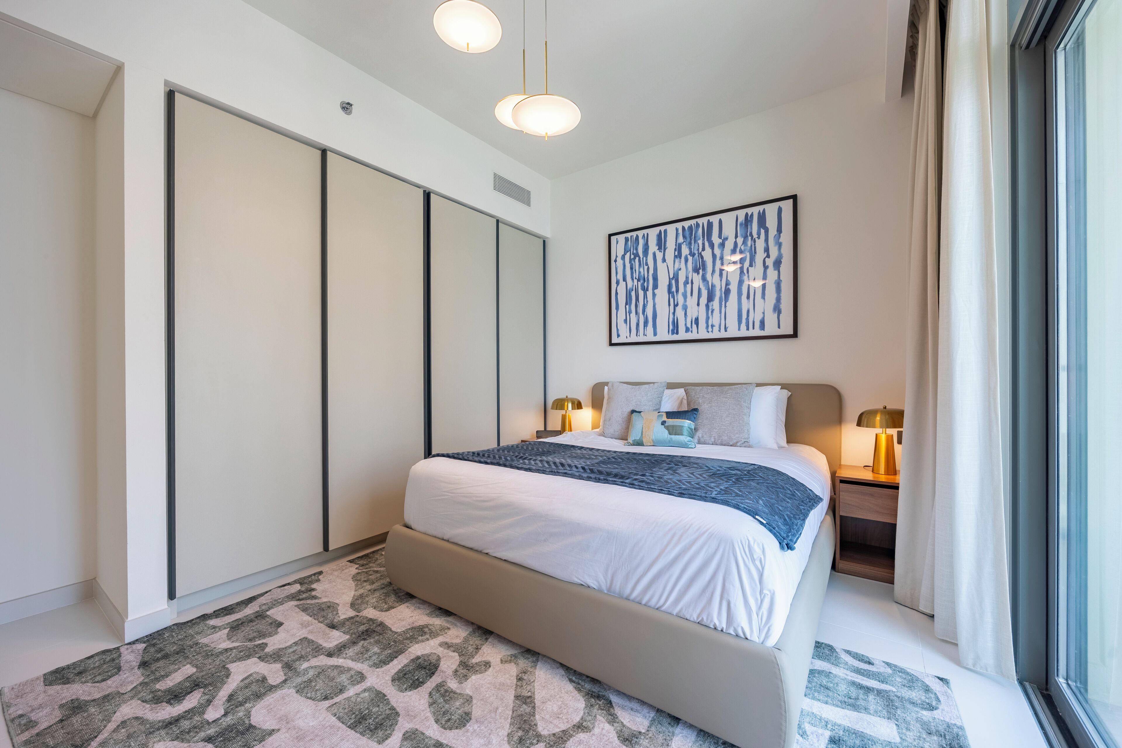 Une chambre moderne avec un grand lit, une armoire, une table de chevet avec une lampe et une fenêtre avec des rideaux.