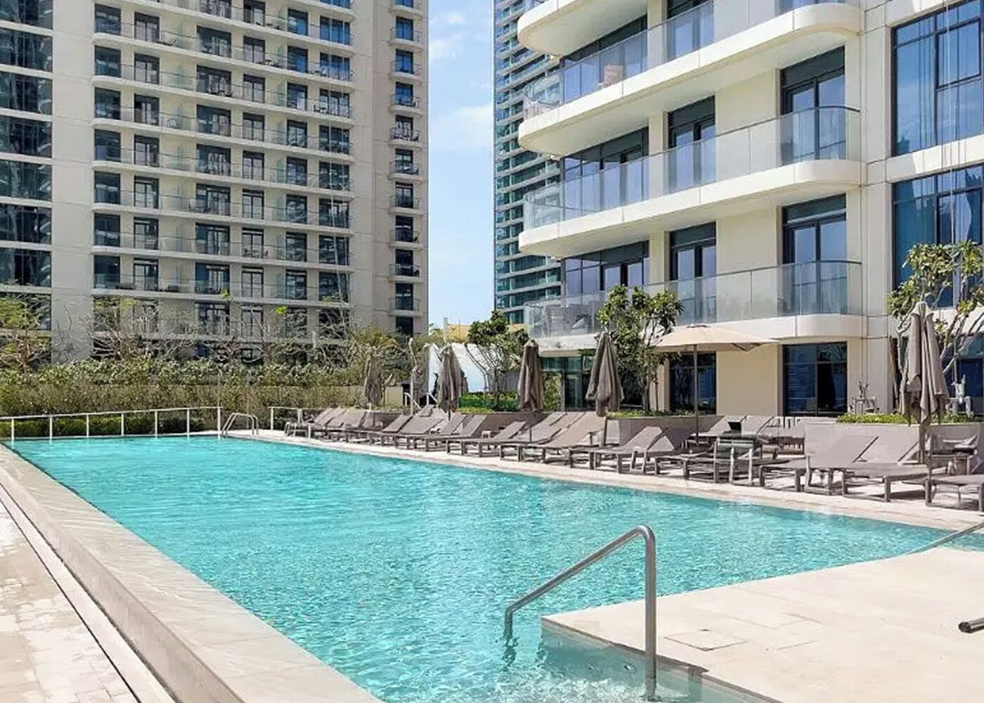 A swimming pool with lounge chairs and umbrellas, surrounded by high-rise buildings.