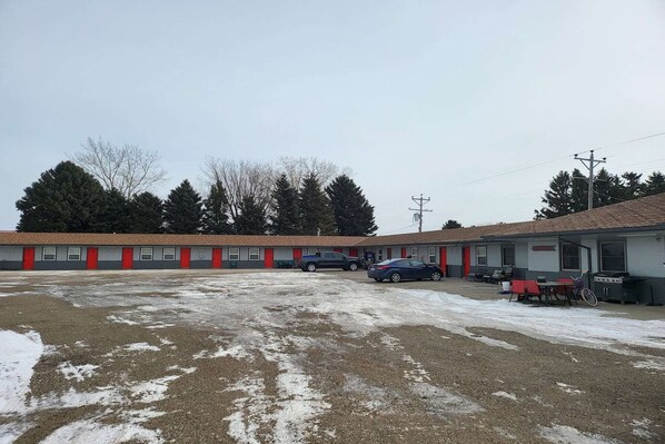 Un motel con estacionamiento, un edificio de puertas rojas y algunos coches aparcados.