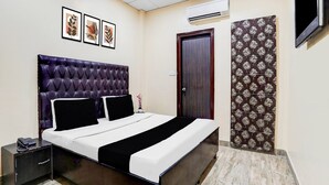 A bedroom with a tufted headboard, a bed with black and white bedding, a nightstand with a phone, an air conditioner, a door, and a patterned curtain. - Saver Double Hotel R1 Inn (Jalandhar)
