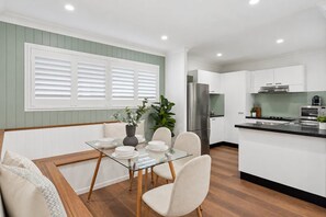 A modern kitchen with white cabinetry, a stainless steel refrigerator, and a glass dining table with chairs. - Unit 6 Nirvana (Sunshine Coast)