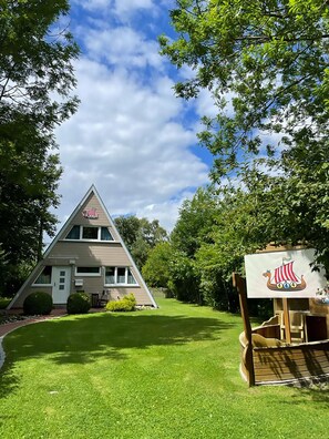 A triangular building with a flag, surrounded by a well-maintained lawn and trees. - Cozy vacation home in a quiet location, ideal for families (Damp)
