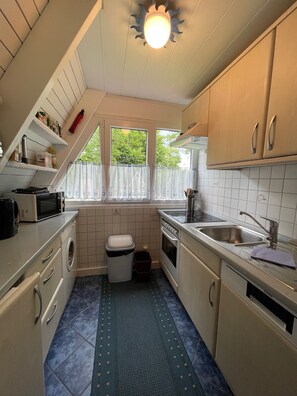 A compact kitchen with a washing machine, microwave, sink, and stove. - Cozy vacation home in a quiet location, ideal for families (Damp)