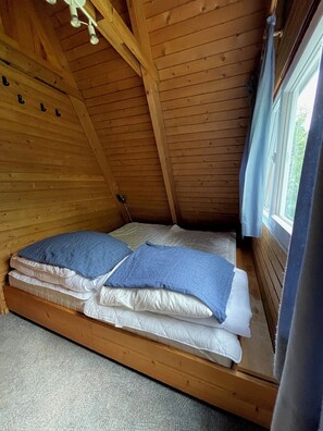 A wooden bunk bed with two pillows, a window with curtains, and a wooden ceiling. - Cozy vacation home in a quiet location, ideal for families (Damp)