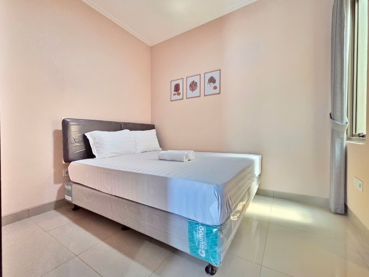 A single bed in a room with a headboard, a window with curtains, and three framed pictures on the wall.