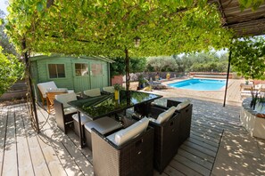 Eine Holzterrasse mit Gartenmöbeln, einem Pool und einem grünen Schuppen.