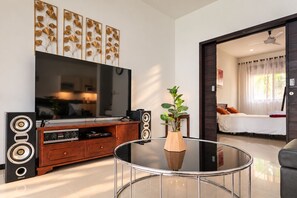 Un salon moderne doté d’un téléviseur à écran plat, d’un meuble de rangement en bois et d’une table basse en verre agrémentée d’une plante.