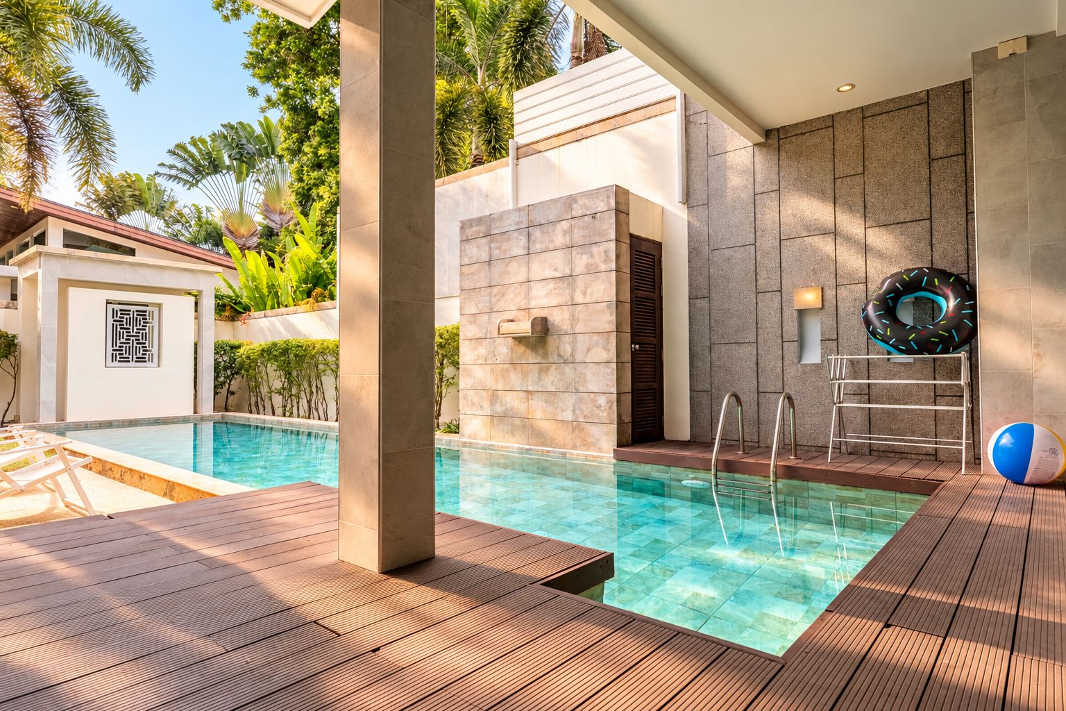 A modern outdoor pool area with clear water, wooden deck, and a stone wall.