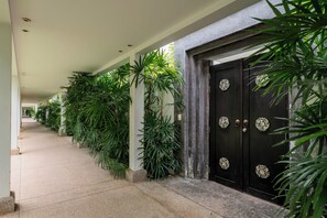 Un couloir bordé de plantes luxuriantes, avec une série de portes, chacune ornée d’une poignée décorative.
