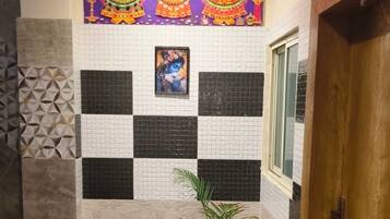 A bathroom with a checkered tile wall, a potted plant, a blue mat, and a wooden door.