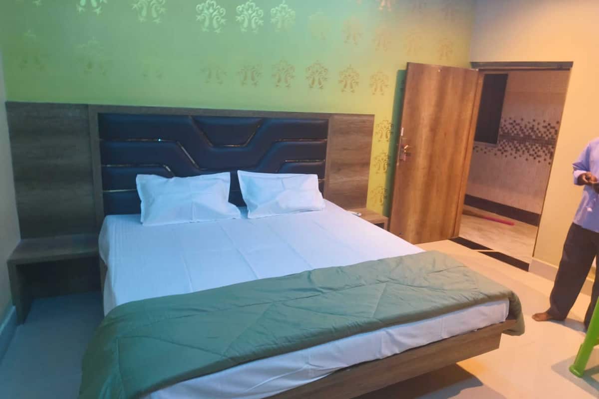 Quarto de hotel com uma cama grande, cabeceira de madeira, parede verde com padrão floral e uma porta com cortina estampada.