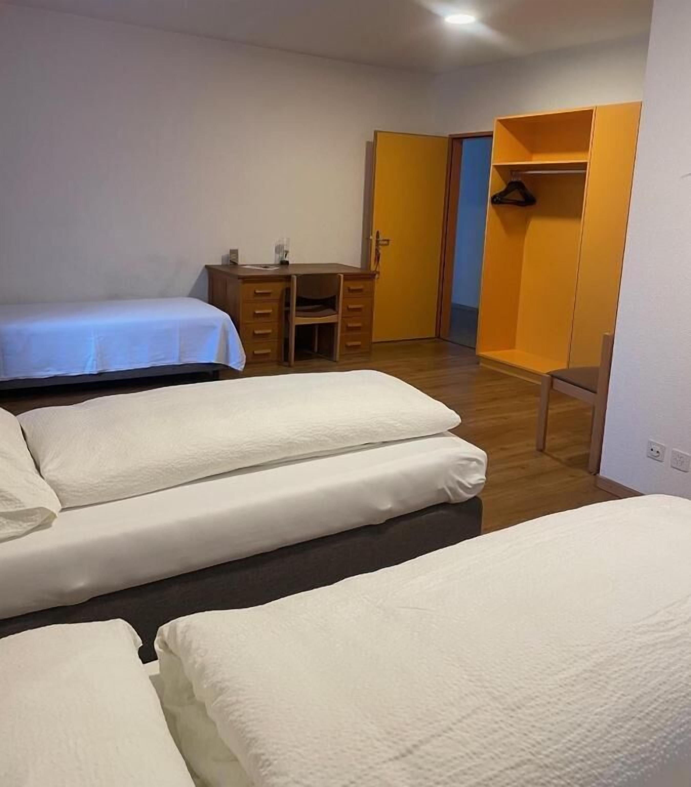 A bedroom with two beds, a desk, and a wardrobe.