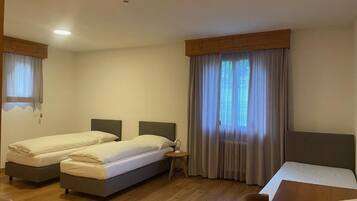 Habitación de hotel con dos camas individuales, piso de madera, una mesita y una ventana con cortinas.