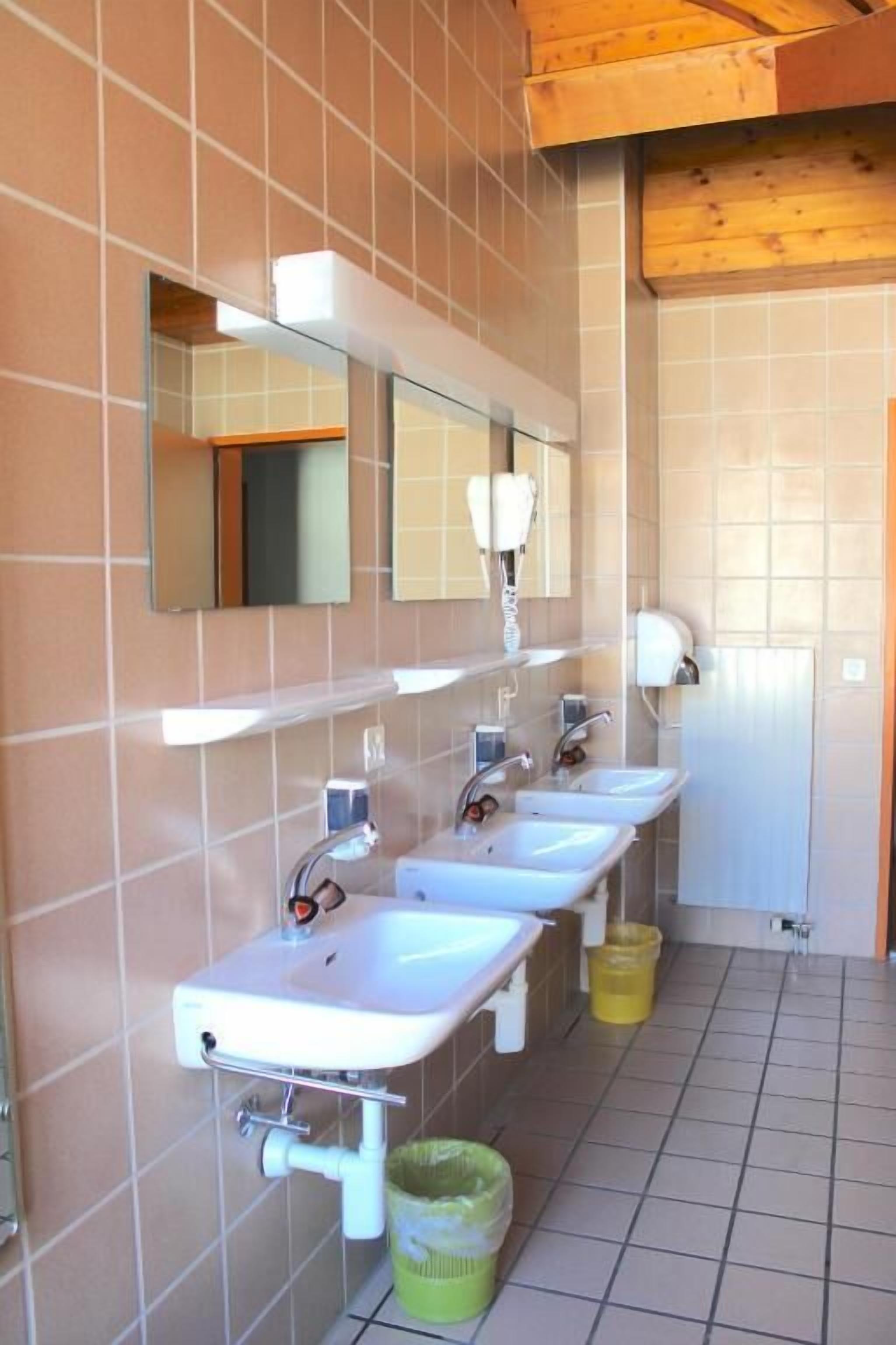 Un bagno con tre lavandini, uno specchio e un cestino.