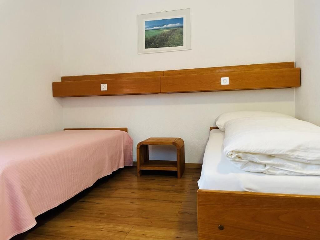 A bedroom with two beds, a wooden headboard, a small wooden stool, and a framed picture on the wall.
