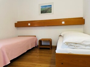 A bedroom with two beds, a wooden headboard, a small wooden stool, and a framed picture on the wall.