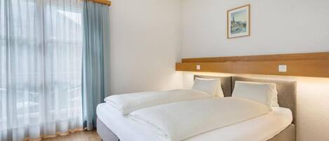 Une chambre d’hôtel avec un lit, des rideaux, une tête de lit et un tableau accroché au mur.