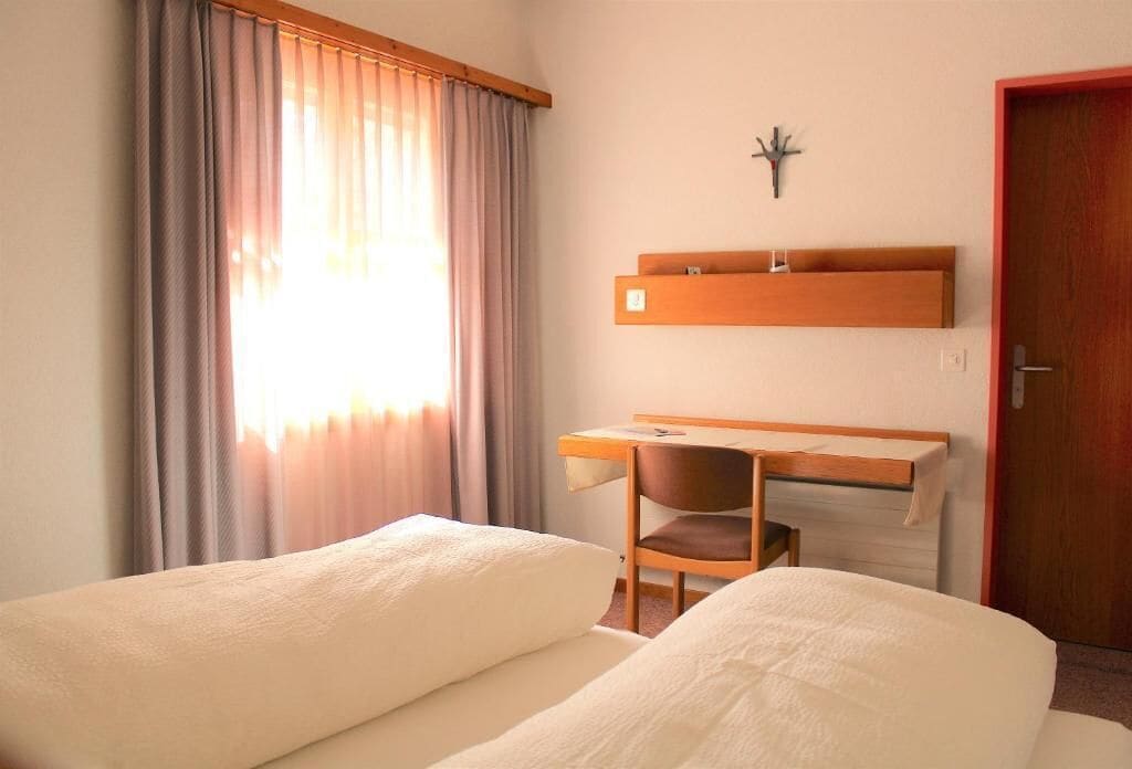 Habitación de hotel con dos camas, un escritorio con silla, un reloj en la pared y una puerta.
