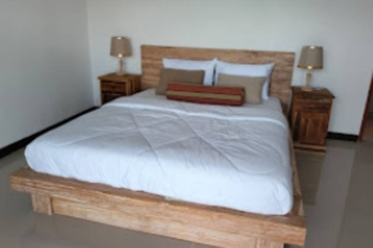 A bed with a wooden frame, white bedding, and two bedside tables with lamps.