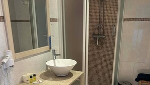 Une salle de bain avec un lavabo blanc, un miroir et une cabine de douche.