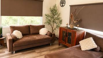 A living room with a brown sofa, a wooden cabinet, a potted plant, and a wall-mounted tree decoration.