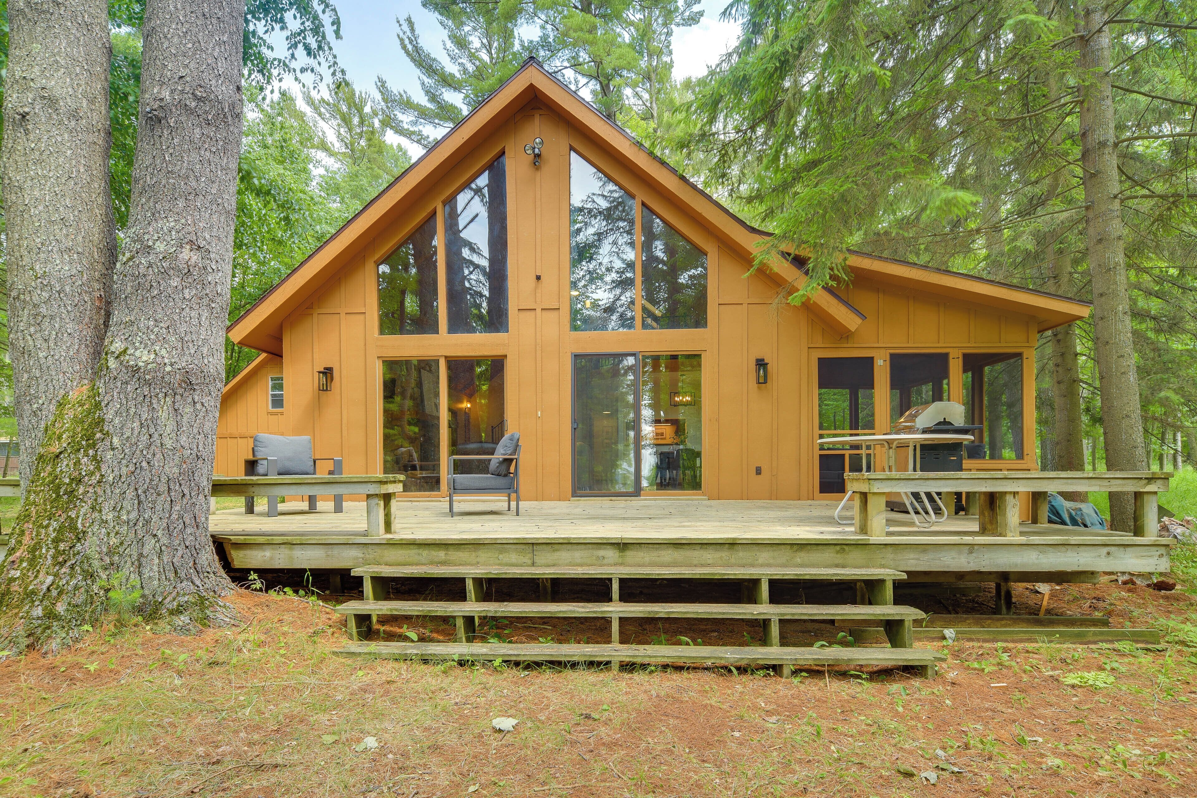 A wooden cabin with large windows, a deck, and a picnic table.