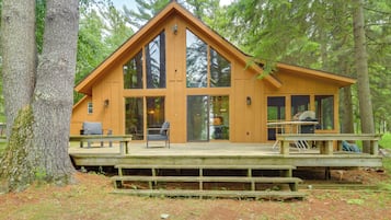 A wooden cabin with large windows, a deck, and a picnic table.