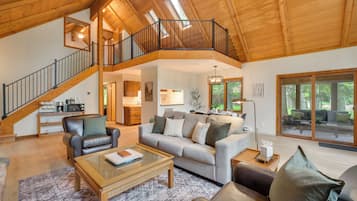A spacious living area with a high ceiling, a staircase, and a large window overlooking a deck.