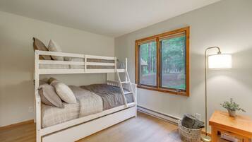 A bunk bed with a ladder, a window with a view of trees, a floor lamp, and a small table with a plant.