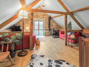 Een knus loft met een stenen muur, houten balken, een rode bank, een open haard en een groot raam.