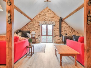 A cozy loft bedroom with a stone wall, wooden beams, a red sofa, a wooden table, and a TV. - 2 bedroom accommodation in Dulverton (Dulverton)