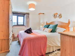 A bedroom with a wooden headboard, a bed with a pink blanket, and a window with curtains. - 2 bedroom accommodation in Dulverton (Dulverton)