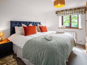A neatly made bed with a blue headboard, white and orange pillows, and a rolled white towel. - 2 bedroom accommodation in Dulverton (Dulverton)
