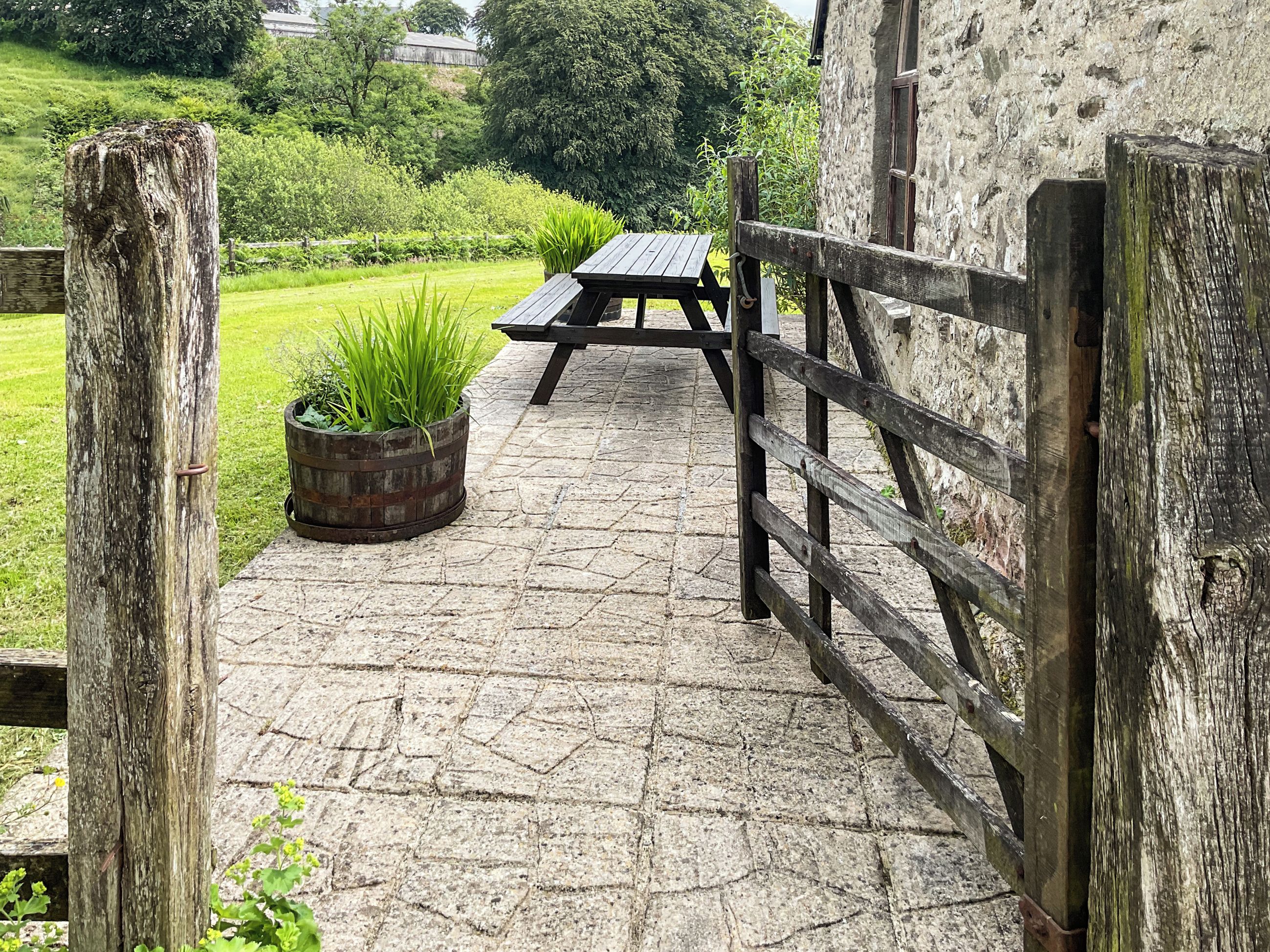A rustic wooden gate leading to a stone-paved patio with a picnic table and a potted plant.