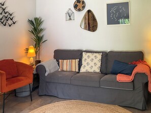 Ein Wohnzimmer mit grauem Sofa, einem roten Sessel, einer Lampe und Wandbildern.