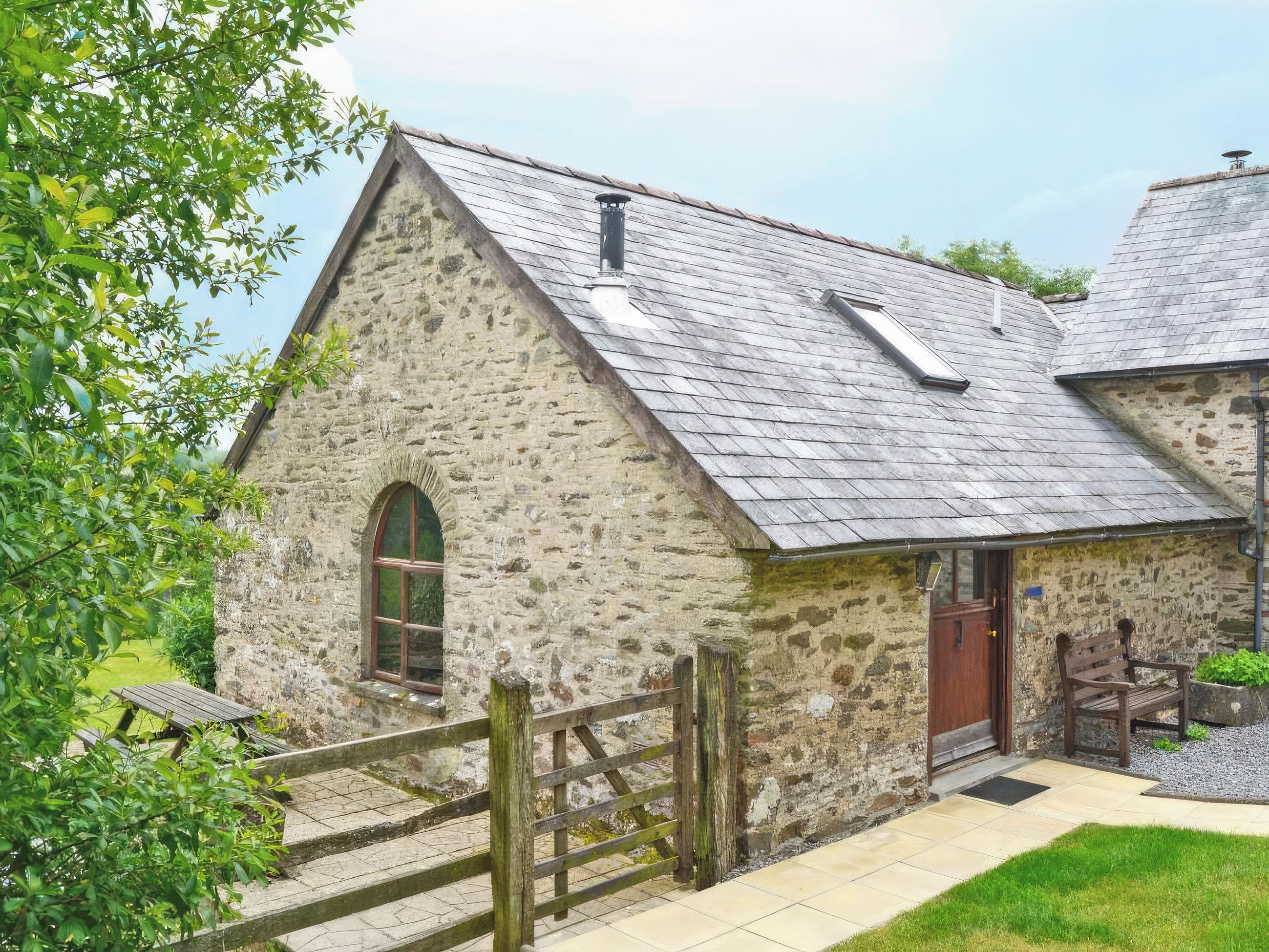 A stone building with a pitched roof, a wooden gate, and a bench.