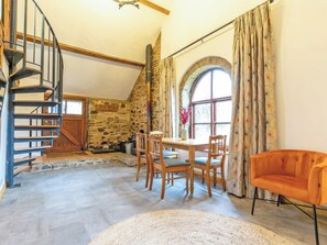 Ein Zimmer mit Steinwand, einer Holztreppe, einem Esstisch mit Stühlen und einem großen Fenster mit Vorhängen.