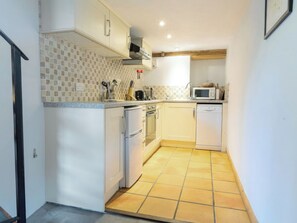 Una cocina compacta con armarios blancos, microondas, lavavajillas y salpicadero de azulejos.