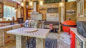 A rustic kitchen with a tiled backsplash, a central island, hanging lights, and a large red grill. - Outdoor Kitchen & Patio Oasis! 5BR Rapid City Home (Rapid City)