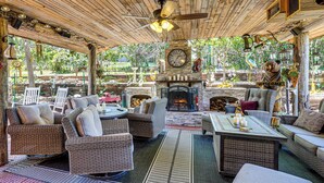An outdoor patio with wicker furniture, a stone fireplace, and a clock on the wall. - Outdoor Kitchen & Patio Oasis! 5BR Rapid City Home (Rapid City)