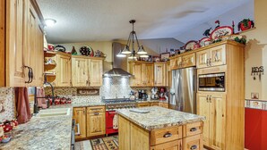 A kitchen with wooden cabinets, a granite countertop, a stainless steel stove, and a refrigerator. - Outdoor Kitchen & Patio Oasis! 5BR Rapid City Home (Rapid City)